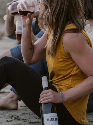 Woman drinking pinot noir on a beach and holding a bottle of Nielson wine